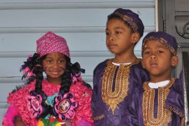 Members of the Young Guardians of the Flame, including a youngster in fuchsia Mardi Gras Indian suit, standing on a porch in the Lower 9th Ward on Carnival Day 2011