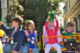 Kids seated atop Mardi Gras parade ladders and holding plush animals thrown to them by float riders.