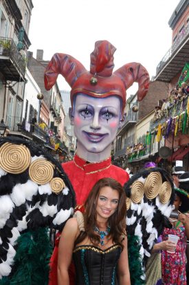 Towering smiling jester along with attractive female reveler with elaborate feathered wings, in the French Quarter on Mardi Gras 2012